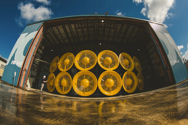A person looks tiny standing next to a wall of 12 giant wind turbines stacked two high.
