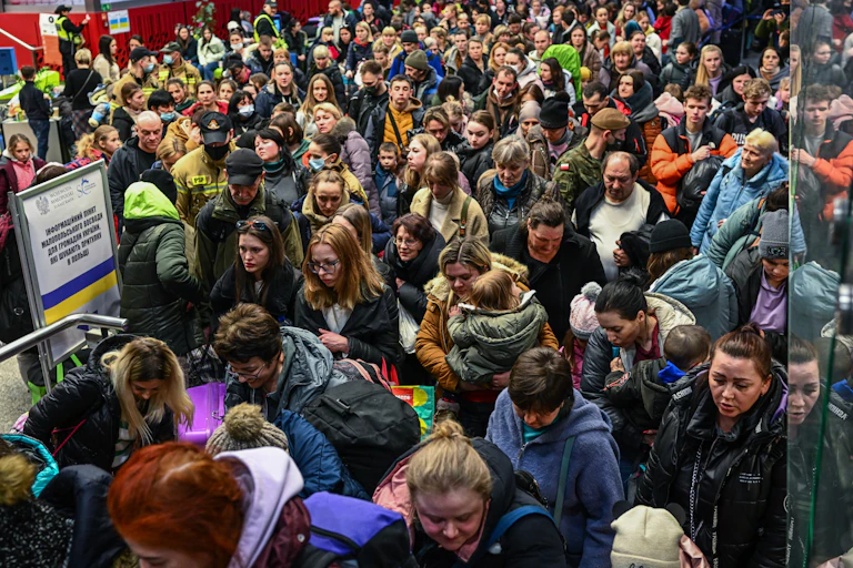 A dense crowd of people walk together in what appears to be a train station