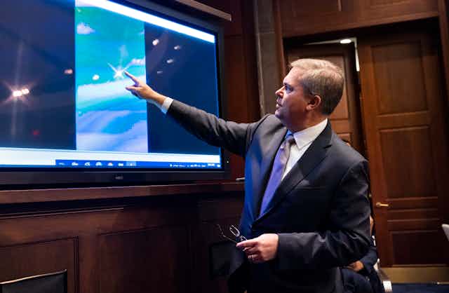 Deputy Director of Naval Intelligence Scott Bray plays a video of an 'unidentified aerial phenomena,' and points to a point on the screen. 