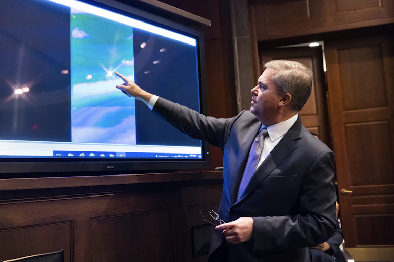 Deputy Director of Naval Intelligence Scott Bray plays a video of an 'unidentified aerial phenomena,' and points to a point on the screen.