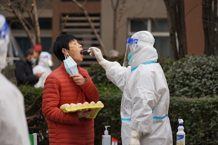 Man in PPE swabbing man on street