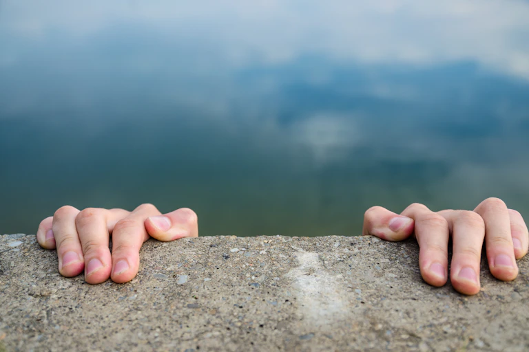 Pair of hands hanging on to the edge of a cliff