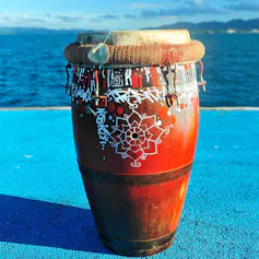 A tall, reddish brown drum sits with water in the background.