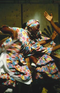 A woman in a bright floral outfit does a traditional dance.