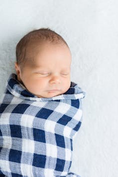 Sleeping baby wrapped tightly in checked blanket