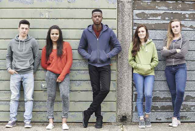 Group of young people leaning on a wall.