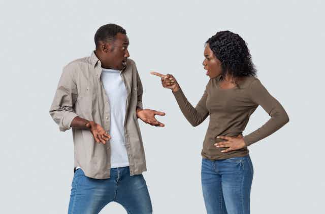 A couple wearing jeans and khaki tops argues against a white background.
