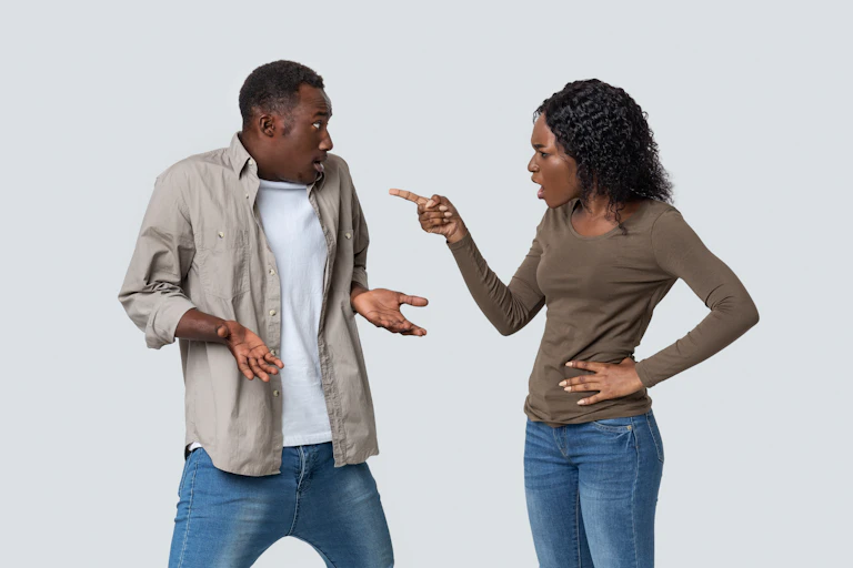 A couple wearing jeans and khaki tops argues against a white background.