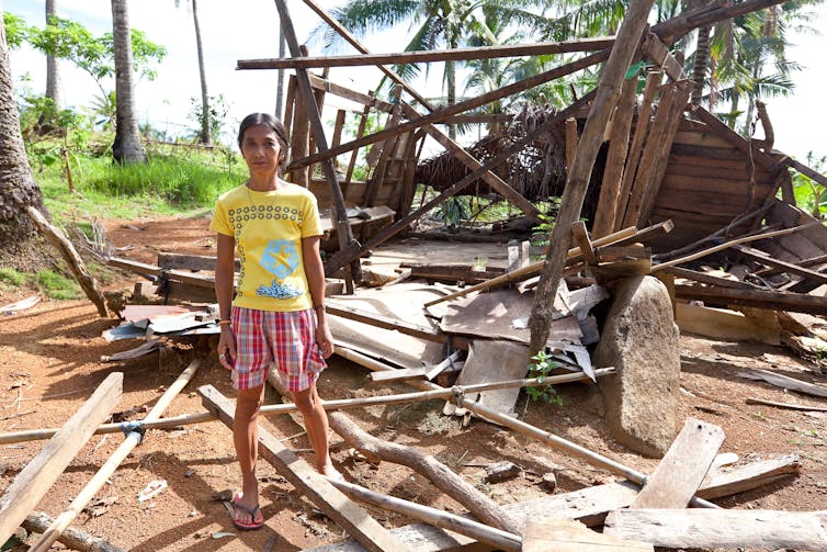 A woman in yellow in front of a devastated house.