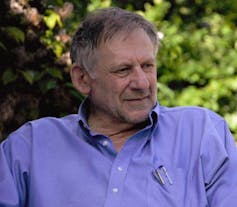 A man in his 70s with gray hair wearing a blue button-down shirt