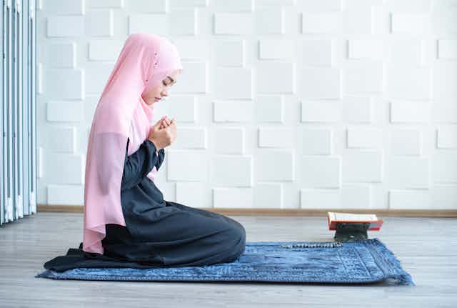 A muslim woman prays on a prayer mat.