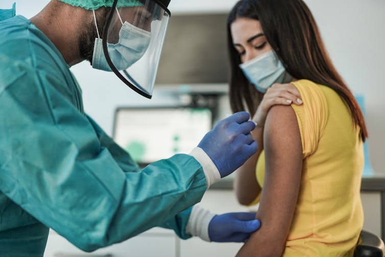 A woman receives a vaccination from a health worker dressed in PPE.