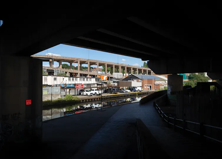 Dark spaces beneath a concrete structure through which you can see the sky and buildings beyond.