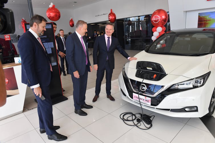 three men stand with electric vehicle