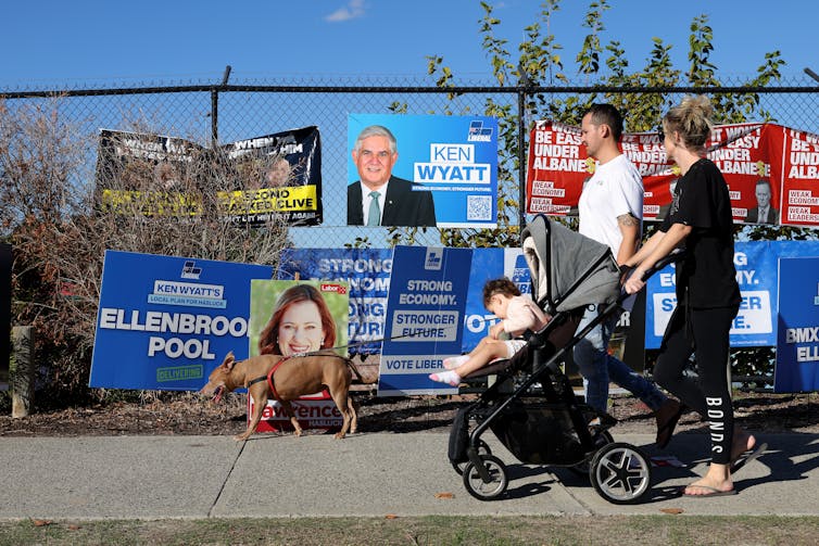 Voters walk past Labor and Liberal signs in Hasluck on election day.