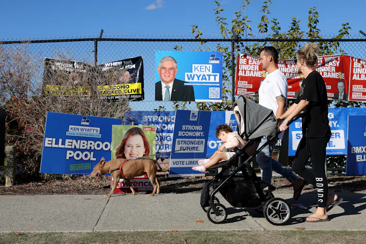 Voters walk past Labor and Liberal signs in Hasluck on election day.