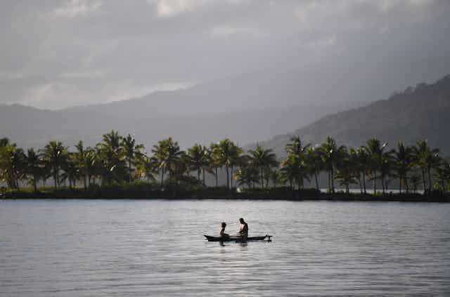 Two people sitting in boat on a lake with rainforest backdrop