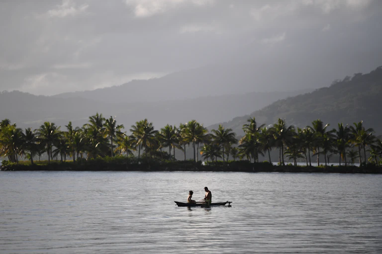 Two people sitting in boat on a lake with rainforest backdrop