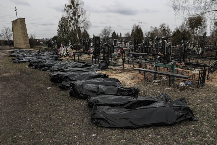 A row of body bags are lined up in front of a graveyard next to a church.
