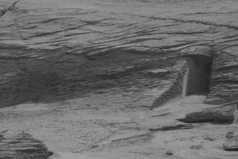 A grainy black and white picture showing rocky terrain and what appears to be a doorway in the rock.