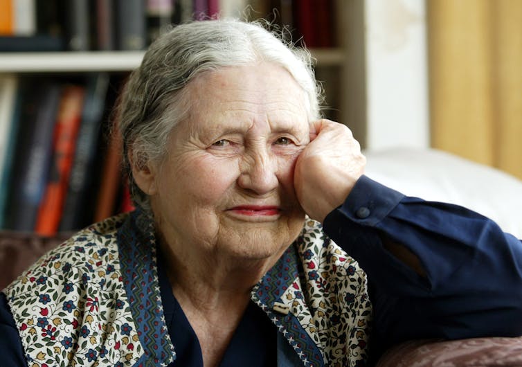 a smiling older woman in a cardigan, in front of a bookshelf