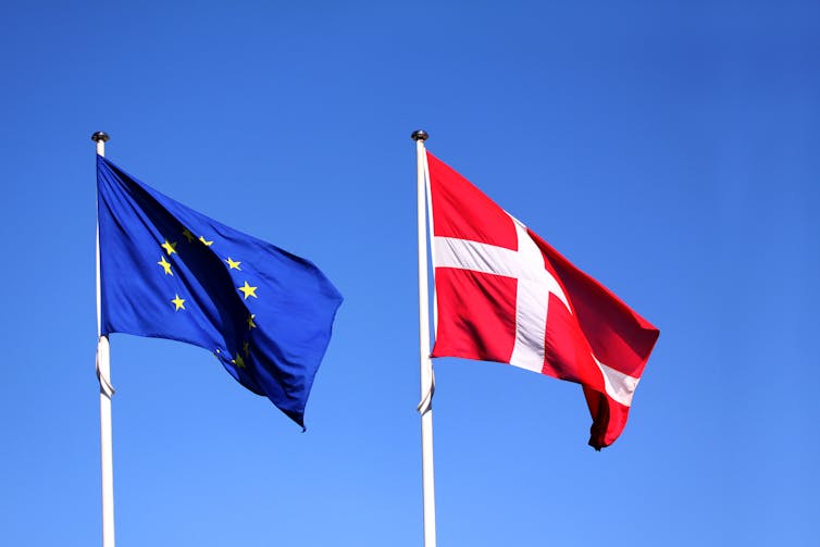 An EU flag and the flag of Denmark flying side by side against a blue sky