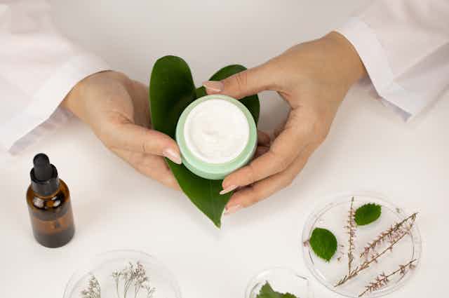 Hands holding a tub of cream with leaves in the background