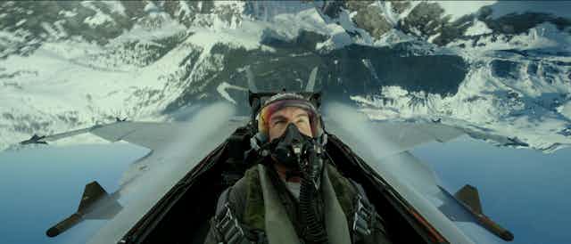 Tom Cruise as Maverick, flies upside down near snowy mountains