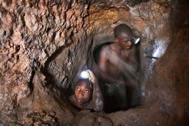Boys with hammers hacking at a rock face in dark deep tunnels 