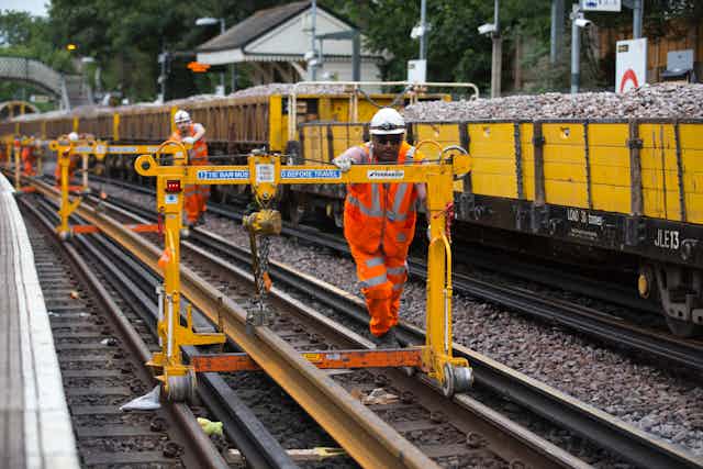 Rail workers in orange hi-vis suits push structures on rail tracks.