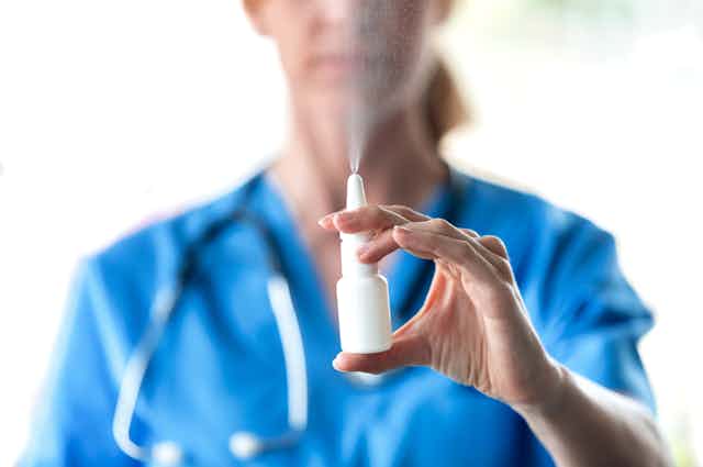 A health-care worker sprays a nasal spray into the air.