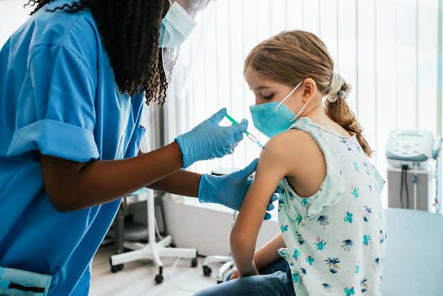 Young girl watching her being injected with COVID-19 vaccine at a medical clinic.