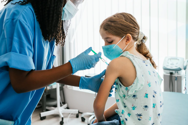 Young girl watching her being injected with COVID-19 vaccine at a medical clinic.
