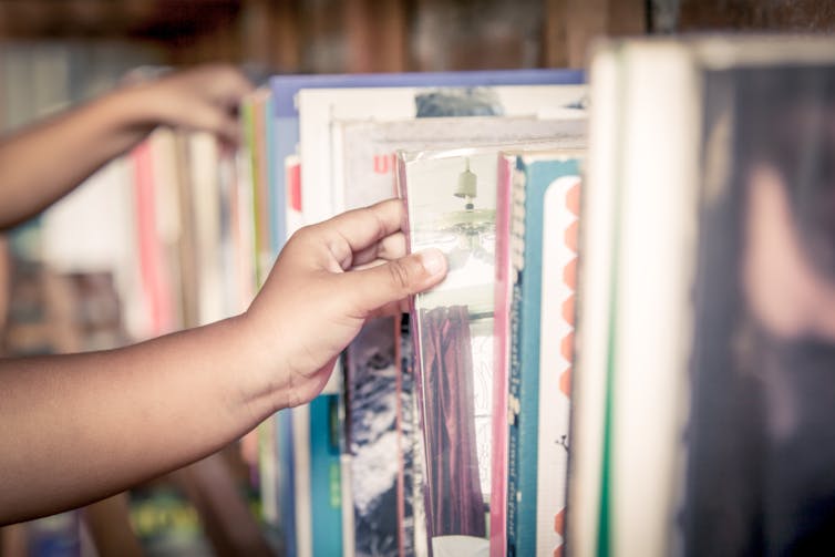 A child's hand is seen reaching for a book.