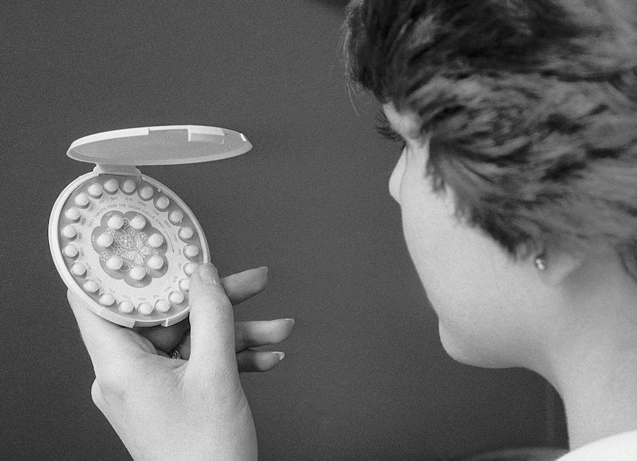 A woman facing away from the camera holds a carton of birth control pills.