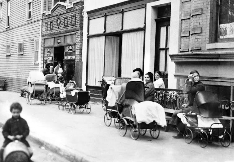 A black and white photograph shows women with baby carriages lined up on a street.