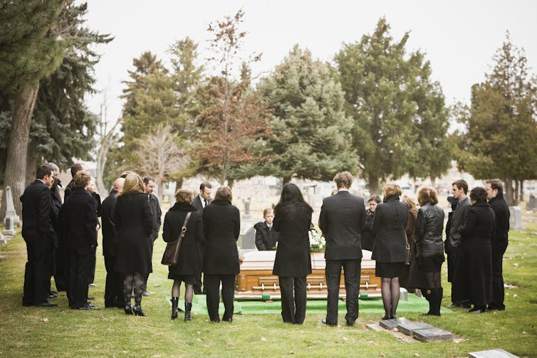 Des gens en noir debout autour d'un cercueil sur une tombe.