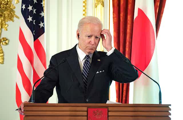 President Joe Biden scratches his head while at the podium with a translation earpiece in.