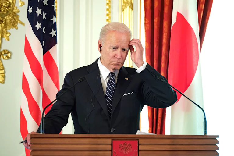 President Joe Biden scratches his head while at the podium with a translation earpiece in.