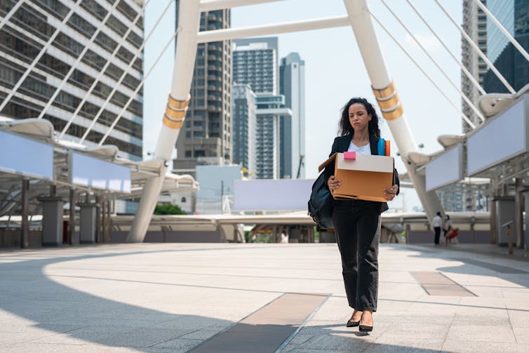 A female office worker carries the contents of her desk in a cardboard box after leaving her office.