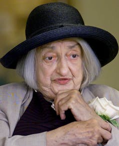 a grey-haired woman in a hat holding a white rose