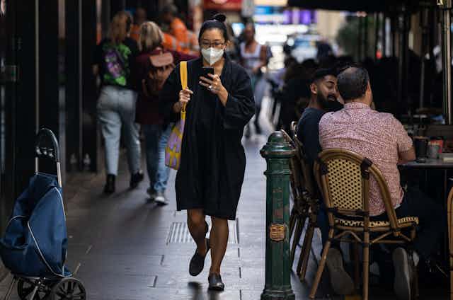 woman with mask walks by cafes