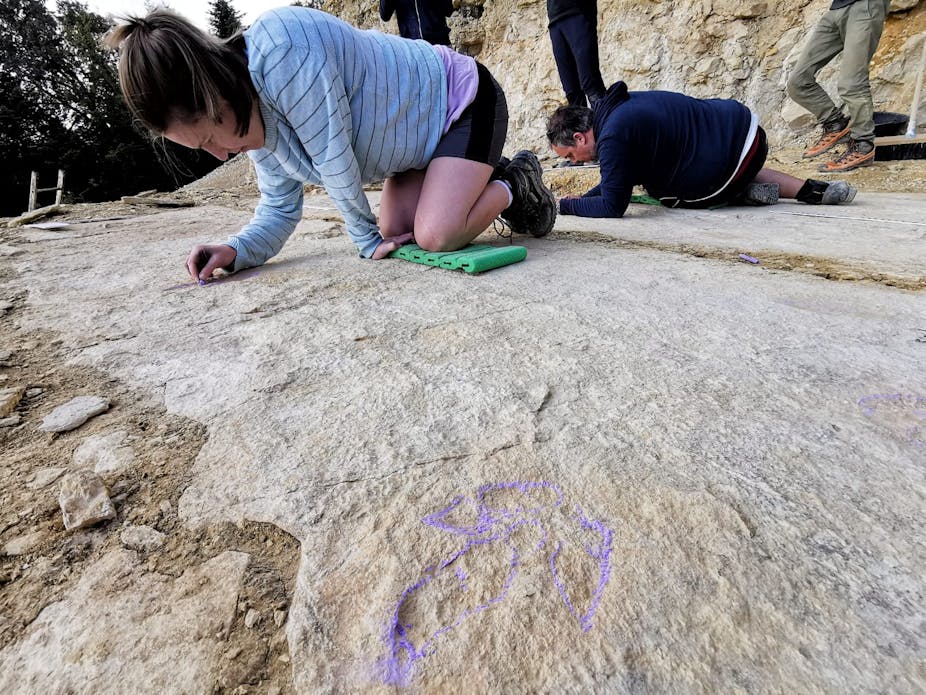 Two people are on their knees, making markings on a large whitish-tan rock slab
