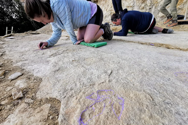 Two people are on their knees, making markings on a large whitish-tan rock slab