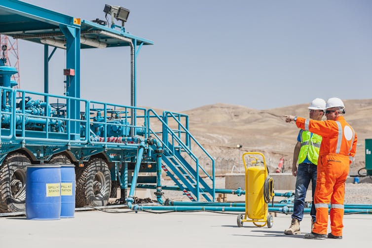 Two people in high vis stand to the right of a blue industrial structure