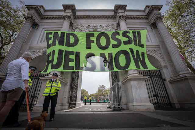 A green banner saying 'end fossil fuels now' is draped over the entrance to Marble Arch in London.