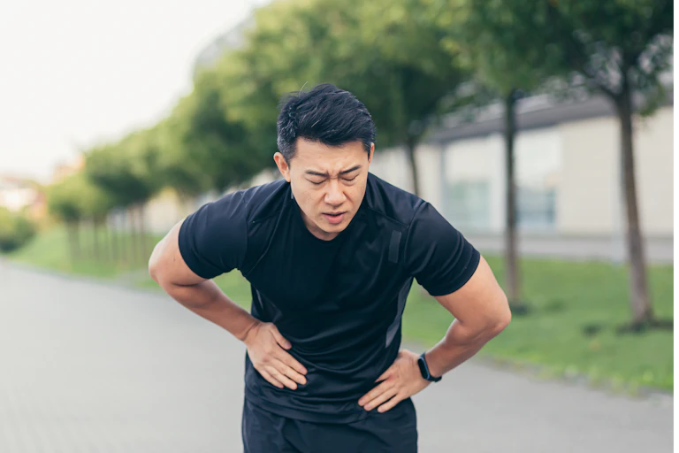 A man wearing workout gear holds his stomach, feeling sick.