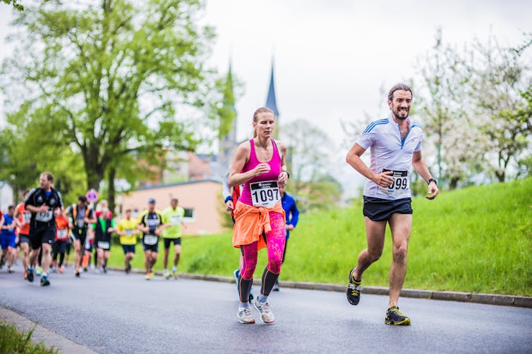 A group of marathon runners racing outdoors. A man and a woman are at the front of the group.