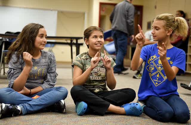 Three young people practice American Sign Language