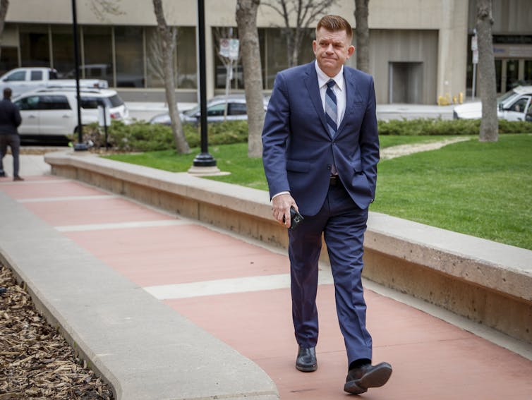 A man in a blue suit walks along a brick pathway.